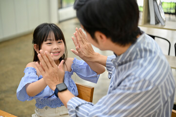 Happy Asian girl giving high-five with her dad, having a happy moment together.