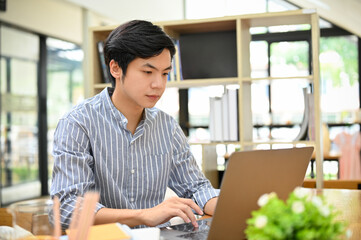 Smart young Asian male freelancer or businessman remote working in the coffee shop, using laptop