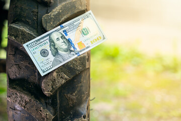 Close-up fresh clean bill of one hundred dollars lies on the tread of a tractor wheel. Farmland...