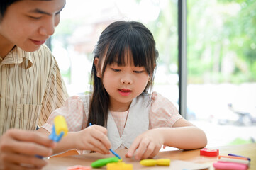 An adorable young Asian girl concentrating learning and sculpting play dough with her dad.