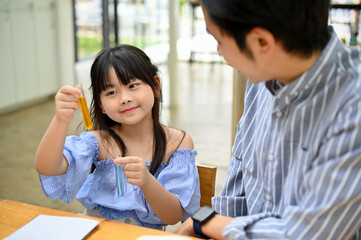 Fototapeta na wymiar Bright young Asian girl holding a test tube, studying science with her school teacher.