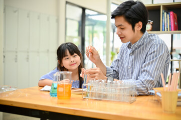 A happy Asian girl concentrates on studying science while her teacher shows the chemical liquid