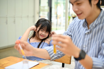 Lovely young Asian girl covering her ears while her teacher doing an exciting chemical experiment