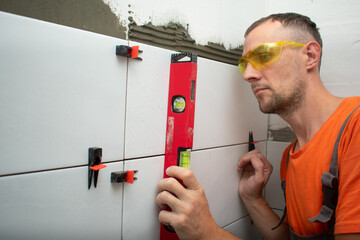 Builder glues tiles on the wall, tile leveling system