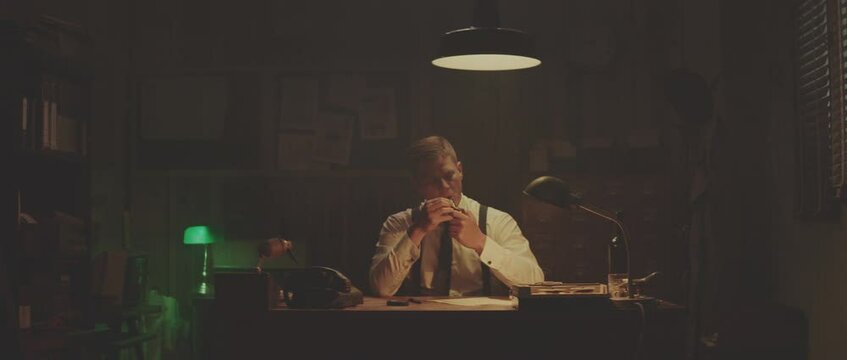 Man in moderately lit room. Sitting at desk, smoking pipe and handling call. Retro style detective using deduction for solving challenging cases.