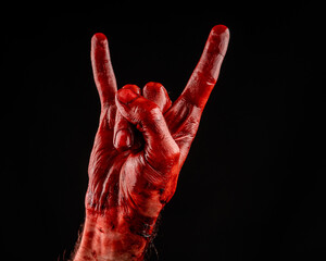 A man's hand covered in blood shows a goat sign on a black background.