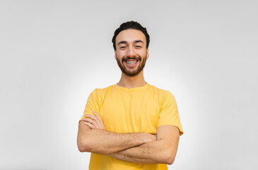 young latin man looking at camera laughing with arms crossed confident posture. white background