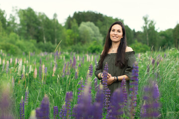 An attractive woman in a field with a summer bouquet of wildflowers Lupinus. Front view.