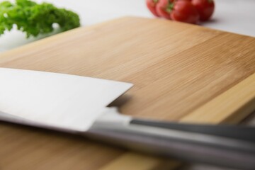 Large knife on wooden chopping board with tomatoes and parsley 