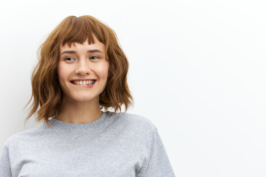 a happy, joyful woman in a gray cotton T-shirt stands against a light background, smiling happily and looking away. Horizontal photo with an empty space for inserting an advertising layout
