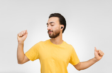 young latin man dances calmly with earbuds true wireless headphones with a surround sound, white background with yellow shirt