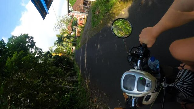 Vertical video, riding motorbike scooter on rural road surrounded by tropical plants