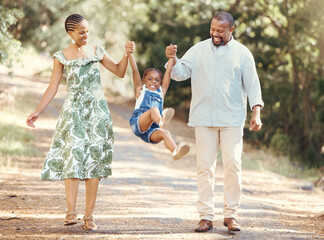 Happy parents swing girl at their hands in the forest during a walk in nature. Cheerful kid having...