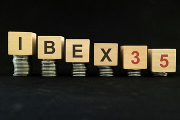 Spanish IBEX 35 stock market index crash and bear market due to financial crisis and recession in Spain. Wooden blocks in with coins in dark black background.