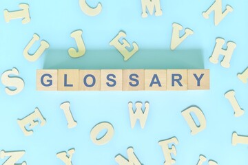 Glossary part of a book concept. Wooden blocks typography word flat lay in blue background.
