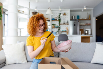 Young satisfied happy woman shopaholic customer sit on sofa unpack parcel delivery box, online...