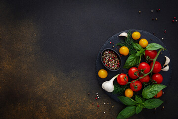 Food background, fresh ripe red and yellow tomatoes, spices and basil leaves, garlic and green onions on a dark board, healthy food concept, copy space, top view