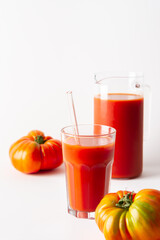 Homemade freshly squeezed tomato juice in a glass and a jug with tomatoes on a white background