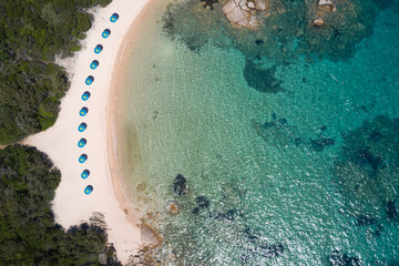 White beaches of Sardinia aerial view. Blue umbrellas along the coastline on the beach top view....