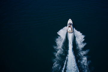 White large open boat with people moving fast on dark blue water top view. White speedboat fast...
