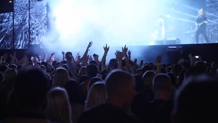 People silhouettes jump waving and clapping hands, crazy dancing with hand-horns at live music concert at open air festival. Fans at favourite rock band performance.