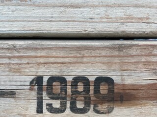 On a weathered wooden board is printed in black paint the number 1989