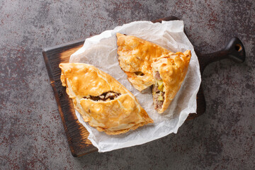 English pies Cornish pasties stuffed with beef, potatoes and swede close-up on paper on a wooden...
