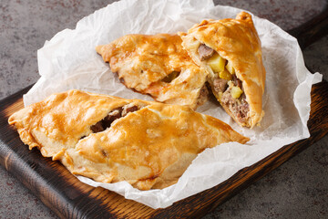 Cornish Pasty Baked pie filled with meat and potatoes closeup on the paper on the wooden board. Horizontal