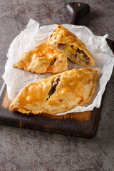 Traditional Cornish pasty filled with meat potato swede and carrot closeup on the paper on the wooden board. Vertical
