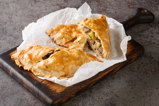 English pies Cornish pasties stuffed with beef, potatoes and swede close-up on paper on a wooden board. horizontal