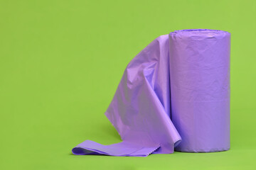 Tightly packed roll of non-recyclable purple rubbish garbage trash bag with the first bag unfolded lime green background 