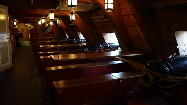 Below decks of old warship featuring cannons and hammock