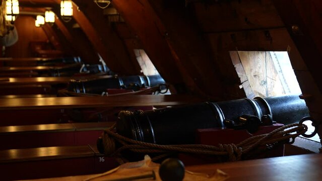 Close up of metal cannons below deck of a wooden old warship