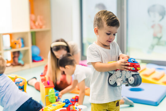 Toddlers boys and their nursery teacher playing with plastic toys and colorful car in a nursery school playroom. Early brain and motor skills development. High quality photo