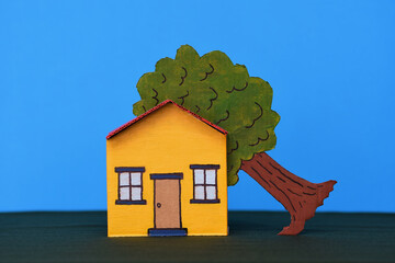 Yellow red toy cardboard house middle of frame dark green base blue background tree in roof