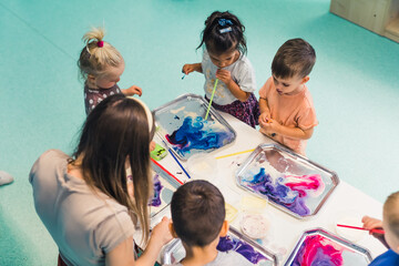 Multicultural group of children at the nursery school milk painting, using pigments for color. Finger paint. High quality photo