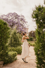 In full growth, young caucasian brunette walks in park on warm summer day. Model wears white summer dress. Relaxation concept