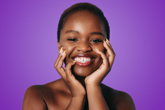 Optimistic African American woman, smiling while touching perfect skin of cheek isolated over purple background. Advertisement for skin cream, anti-wrinkle