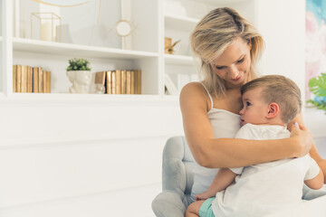 Fototapeta na wymiar Mother and son. Modern living room interior. Beautiful young adult caucasian woman hugging her cute sleepy son. Time for a nap. High quality photo