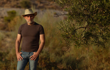 Portrait of adult man in cowboy hat standing in field during sunset