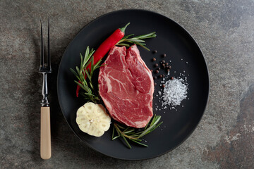 Raw beef steak with rosemary, garlic, salt, and pepper.