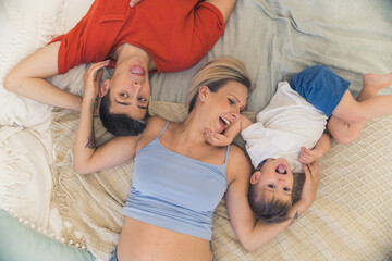 Indoor top shot of cute adorable family of three lying on the bed, joking, and sticking their tongues out. Caucasian married heterosexual couple having fun with their four-year-old son. High quality
