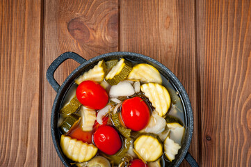 Pickled ripe red tomatoes with zucchini in a bowl on a wooden table surface.