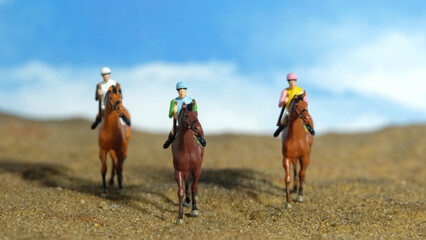 Miniature people toy figure photography. A jockey man riding horse at farm, sand desert land field.
