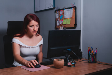Fototapeta na wymiar High quality photography. Annoyed woman working with in an office with her computer. Red-haired woman in a white dress in a travel agency working.