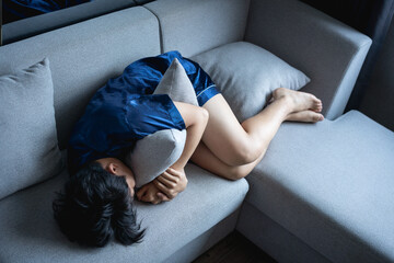 Young man crouching in the sofa and holding a pillow in his arm.