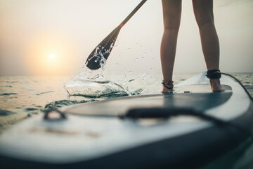 Close up of woman paddleboarding on sunset sea