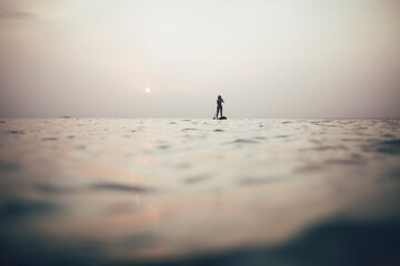 Woman silhouette paddleboarding on sunset sea