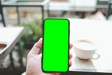 Mockup image of a business people holding smart mobile phone with blank green screen on vintage wooden table in modern cafe restaurant during meeting or lunch.