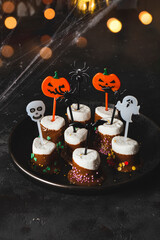  Sweet Halloween treat, marshmallows covered chocolate with sugar and Halloween decorations on a black plate, vertical photo with soft focus, golden bokeh